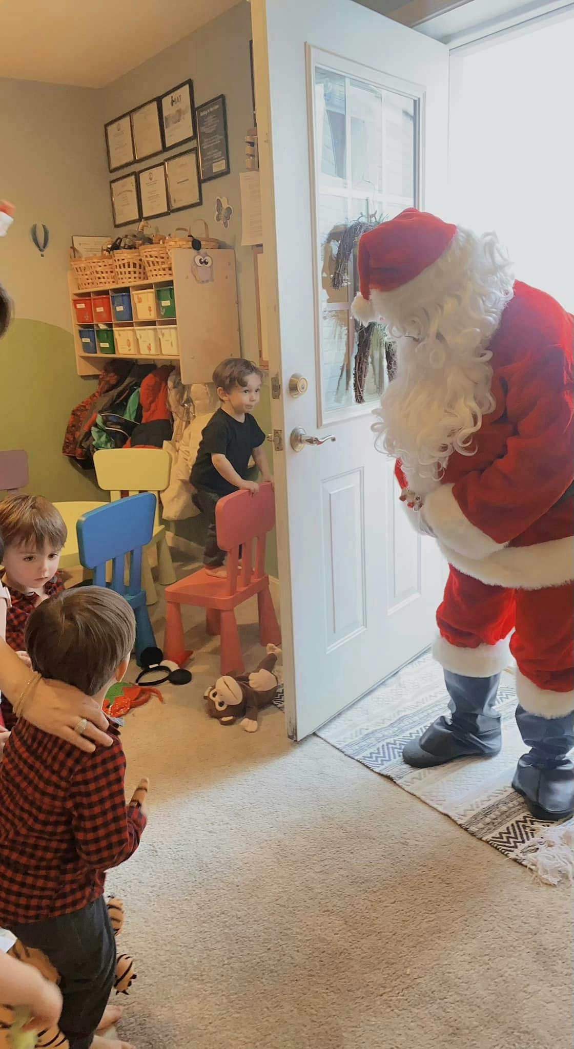 Person dressed as Santa Claus at a doorway with children looking on the other side