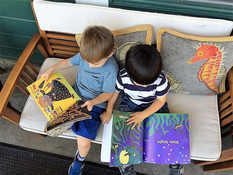 Two children sitting on a bench reading books