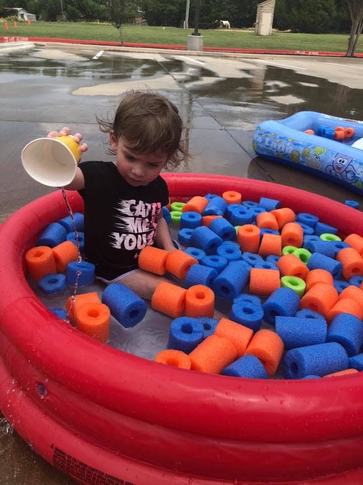 Child in a red inflatable pool filled with blue and orange foam pieces