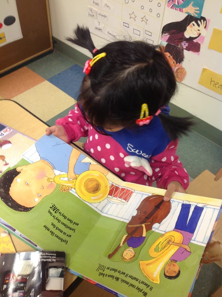 Child with pigtails looking at an open book with illustrations of musical instruments