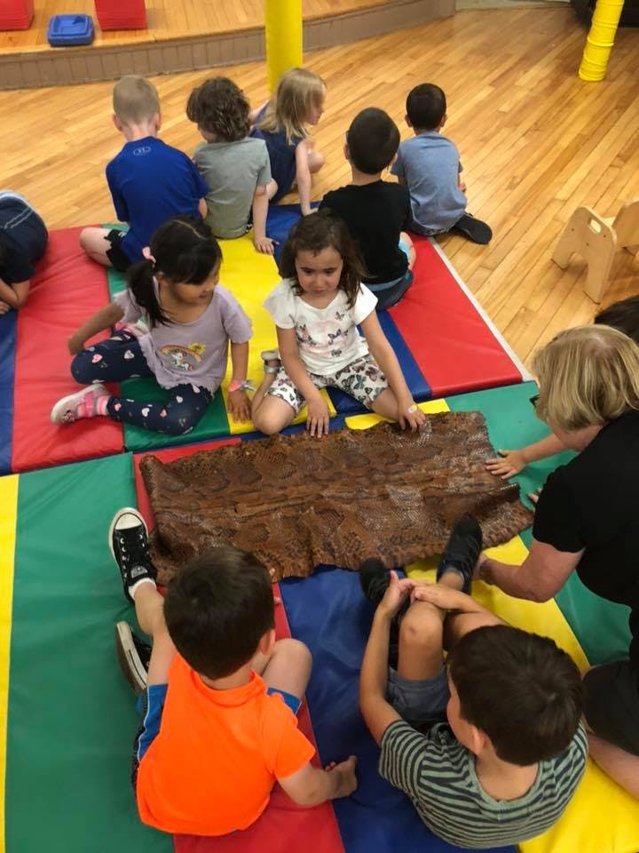 Children and an adult sitting on mats looking at a brown object