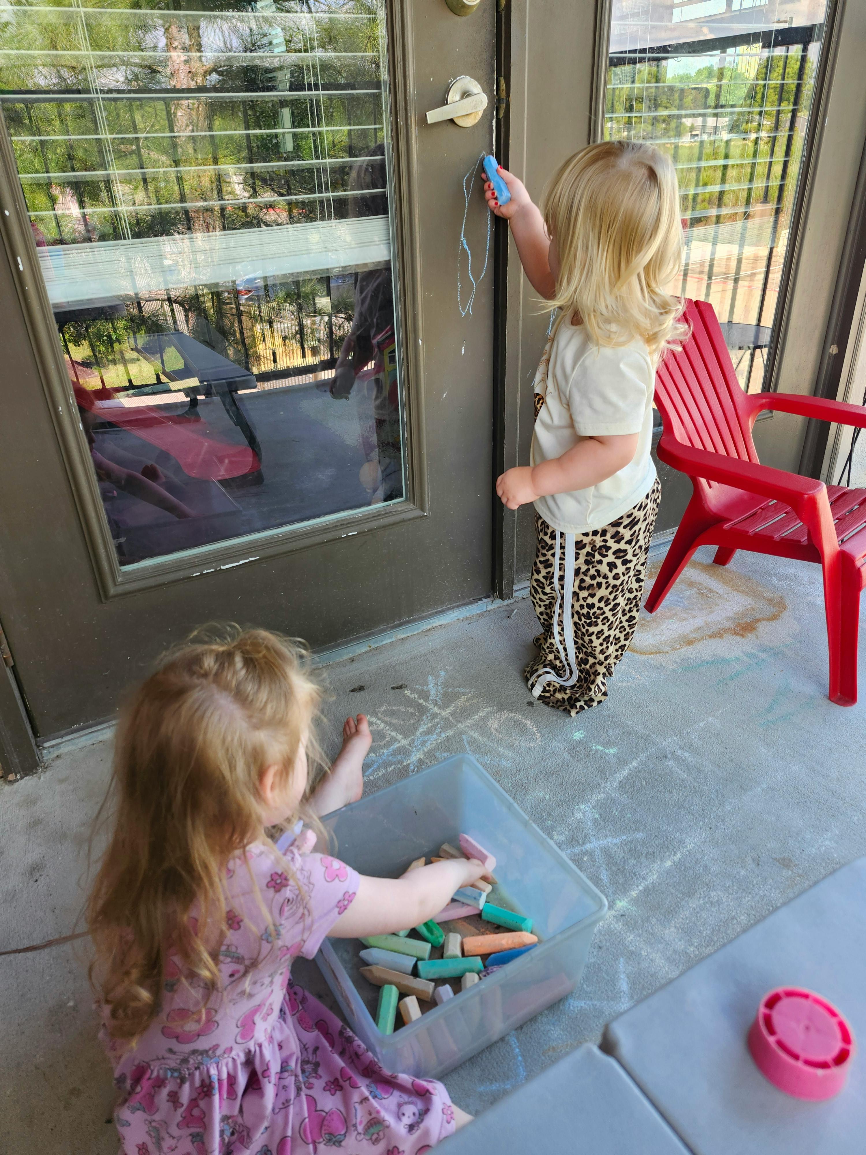 Two children playing with chalk on a patio