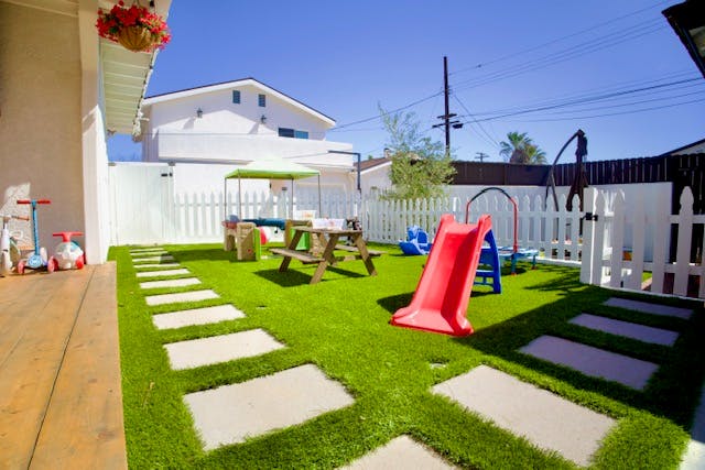 An outdoor playground with artificial turf, a red slide, and a picnic table
