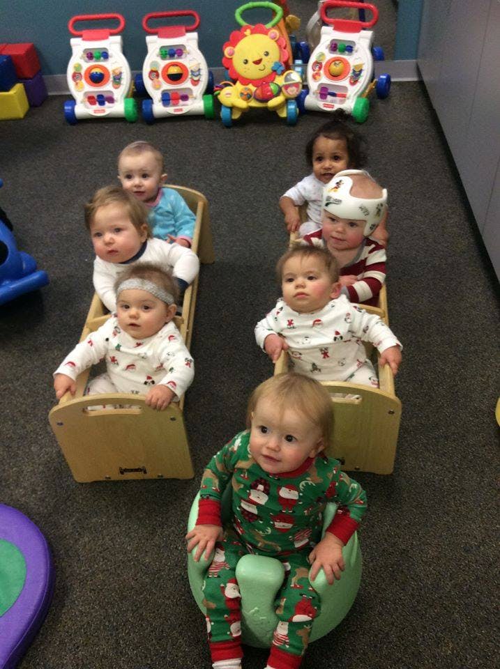 Multiple babies sitting in chairs and on the floor in a room with toys in the background