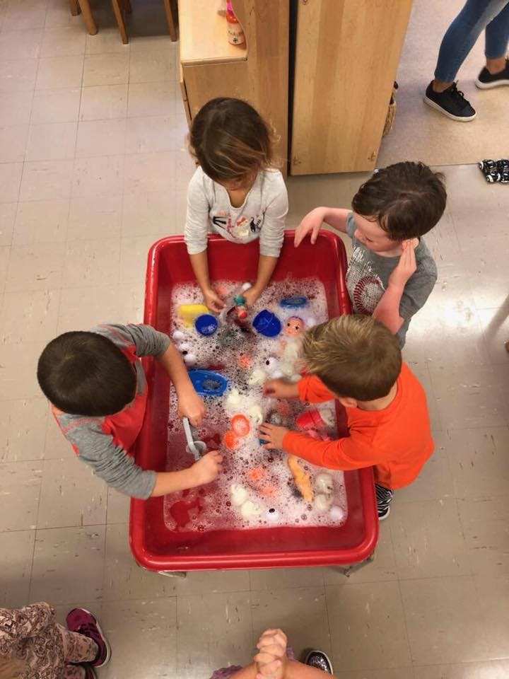 Four children playing with toys in a red bin filled with soapy water