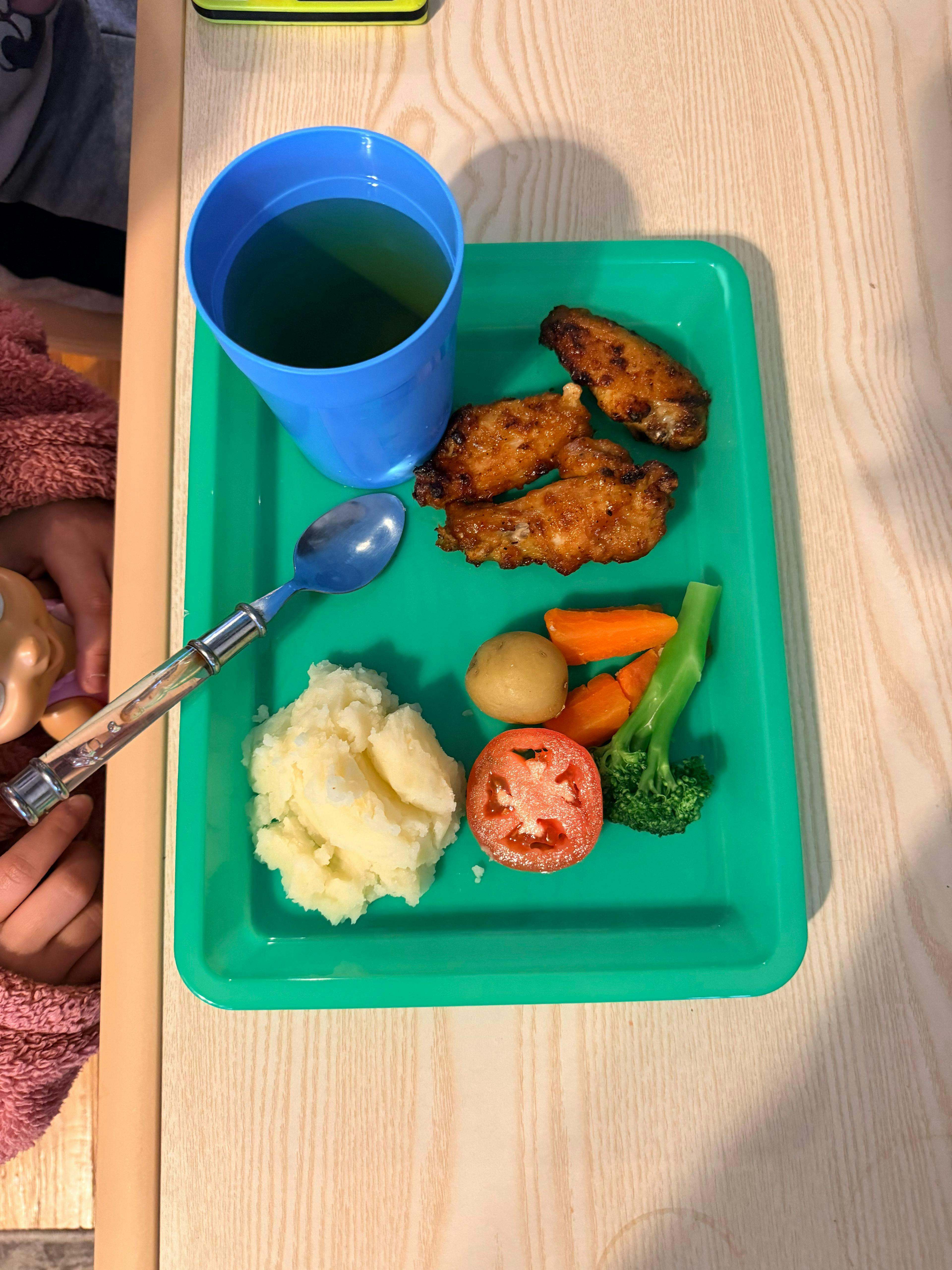A meal with chicken wings, mashed potatoes, and vegetables on a green tray