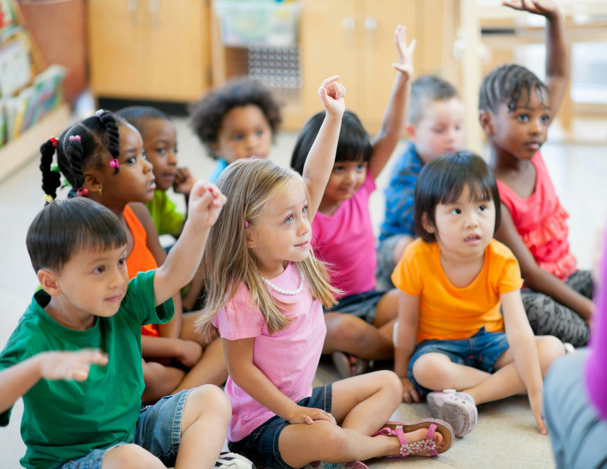 Group of children sitting on the floor, some with hands raised