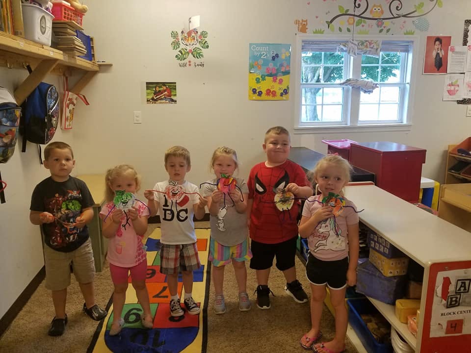 Five children holding up crafts in a classroom