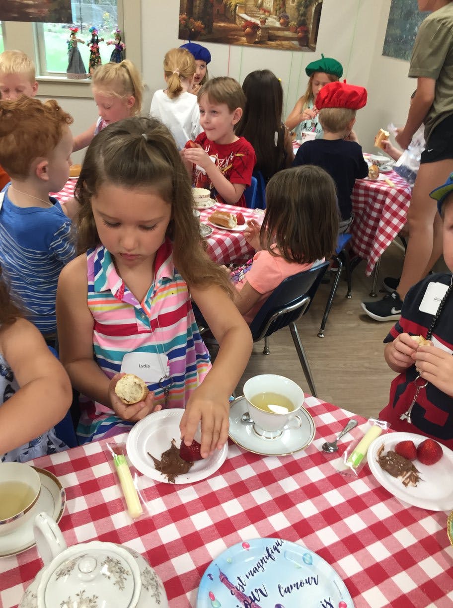 Child dipping a strawberry into chocolate at a table with other children