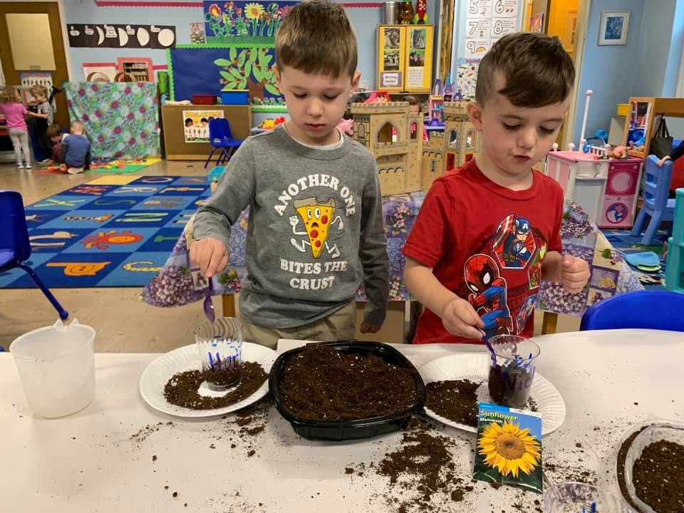 Two children planting seeds in soil at a table