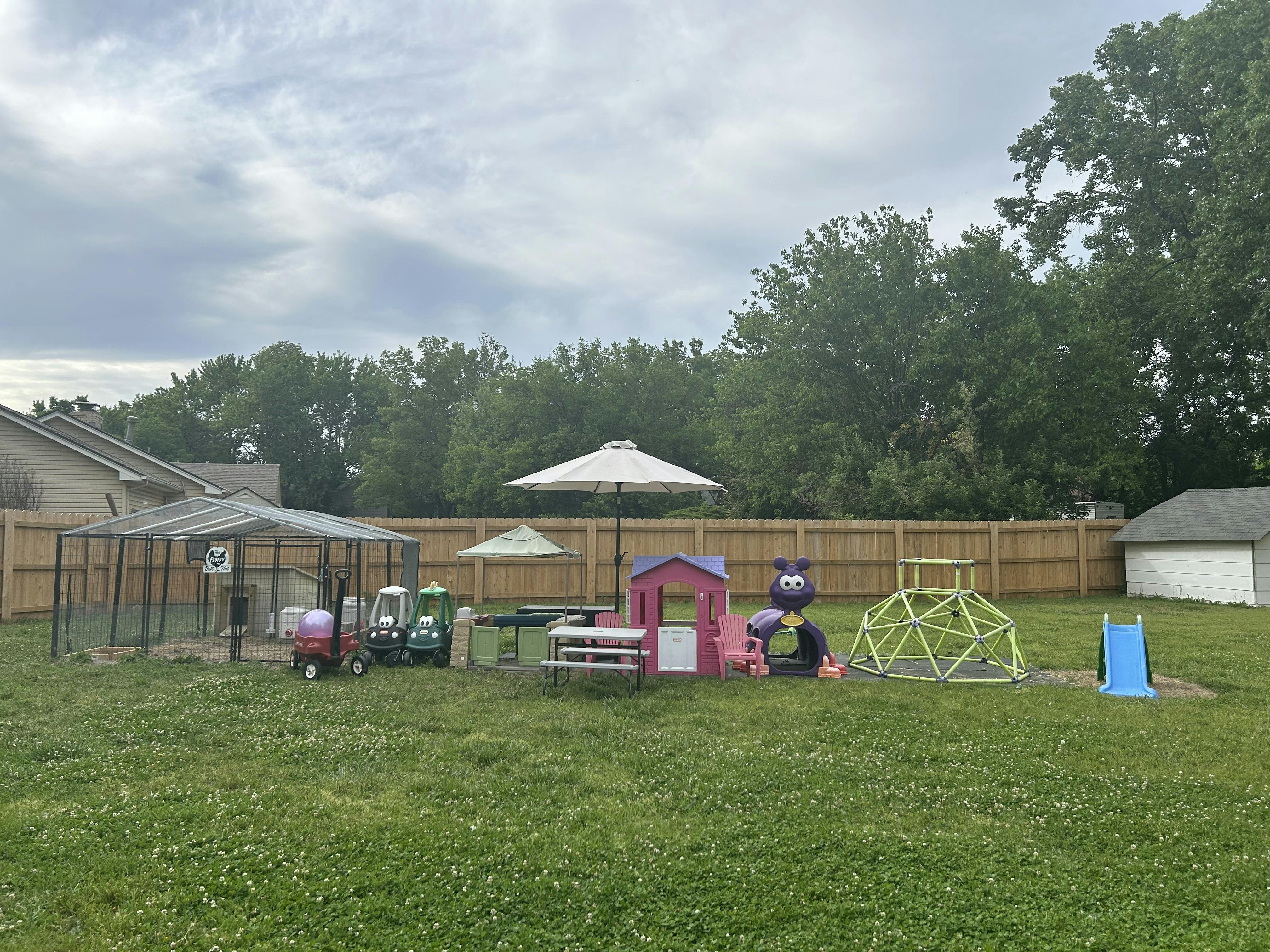 Backyard with play structures, umbrellas, and a fenced enclosure