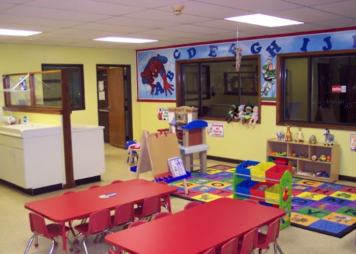 Preschool classroom with red tables and chairs, colorful rug, and alphabet banner