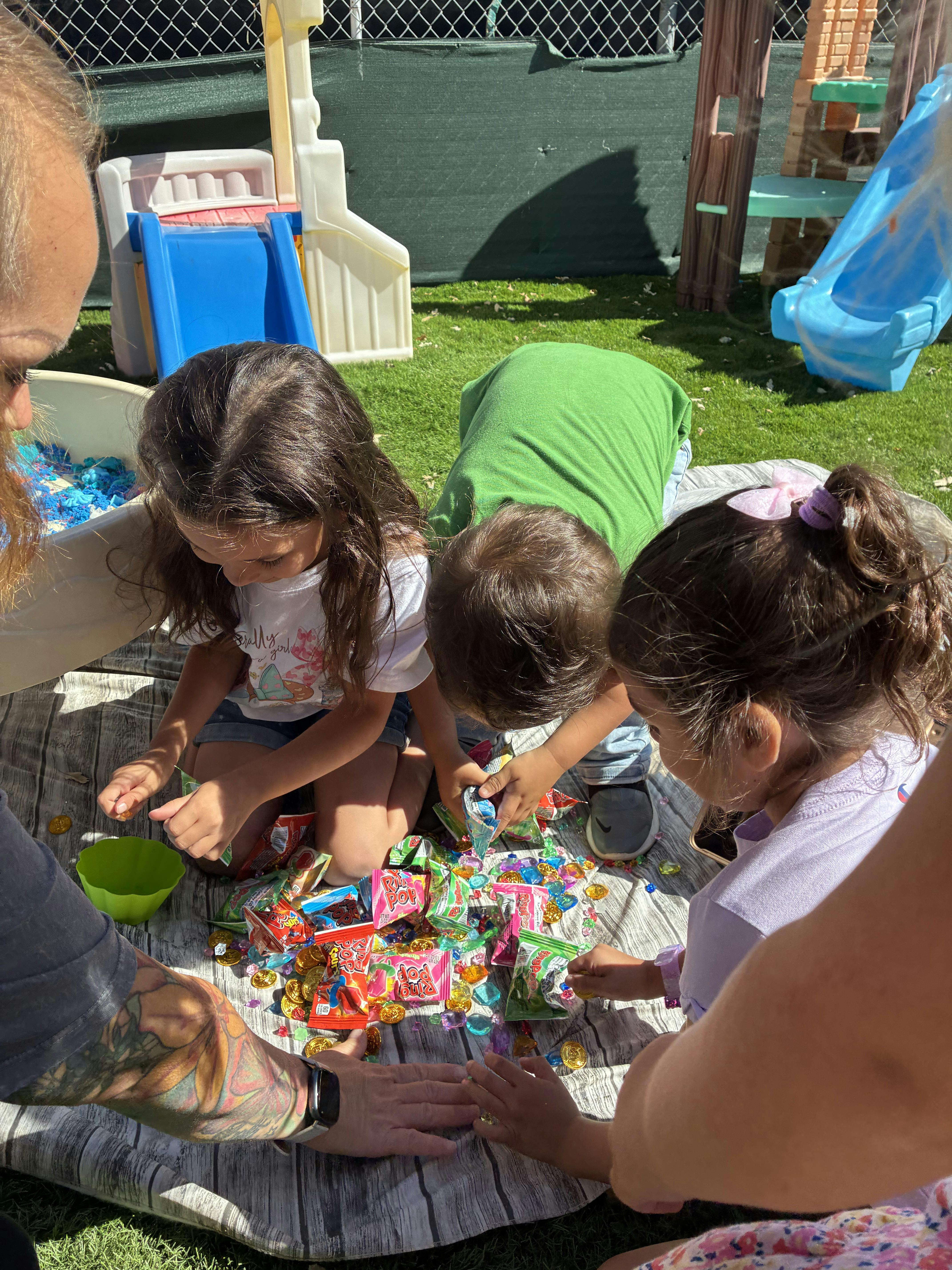 People gathering around a pile of candy and plastic gems on an outdoor blanket