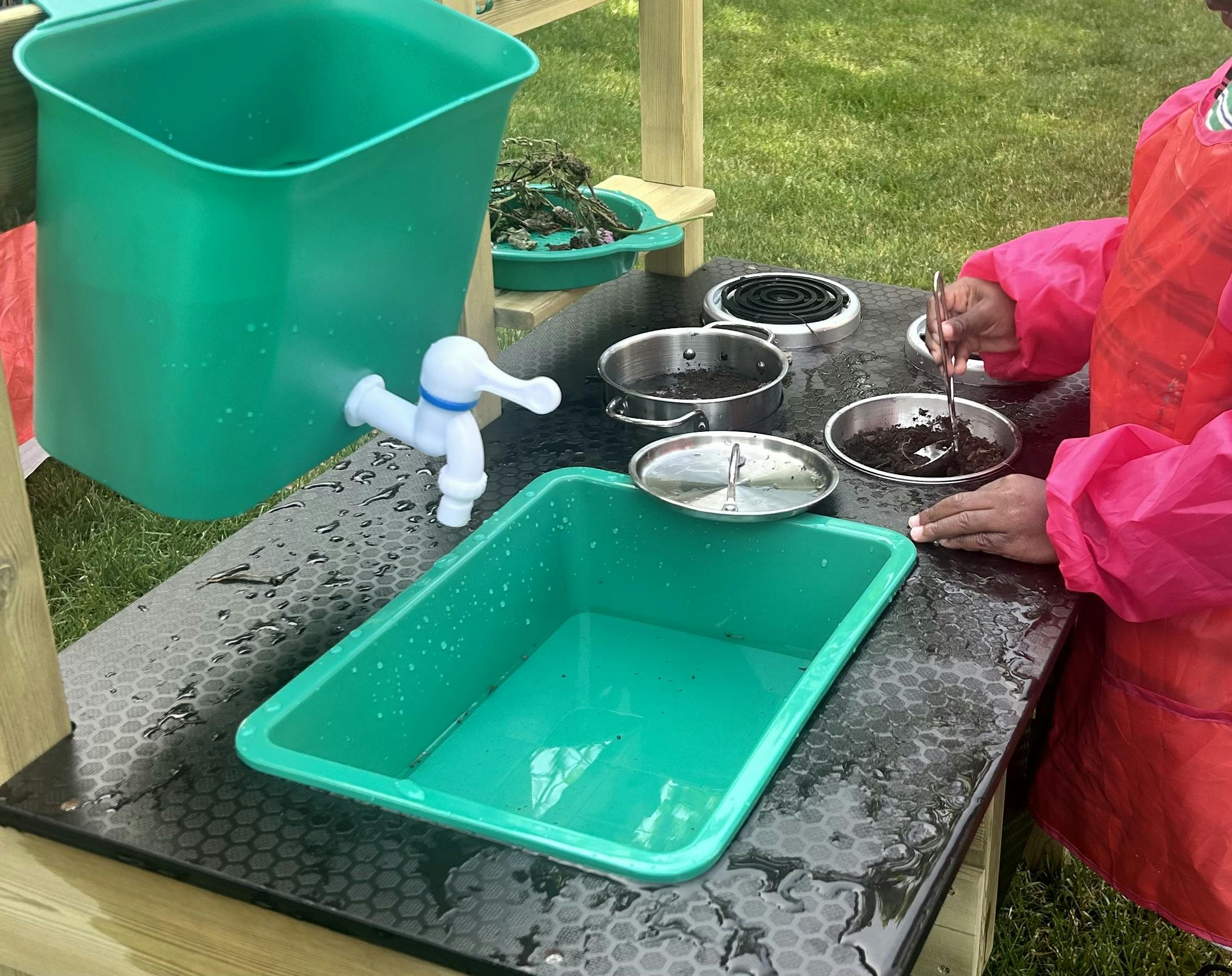 Child in a smock playing with dirt and water at an outdoor toy kitchen