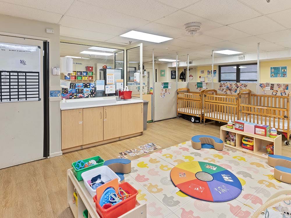 A childcare room with cribs, playmats, and storage cabinets