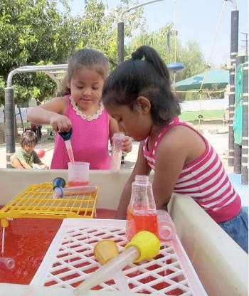 Two children playing with water and droppers in a water table