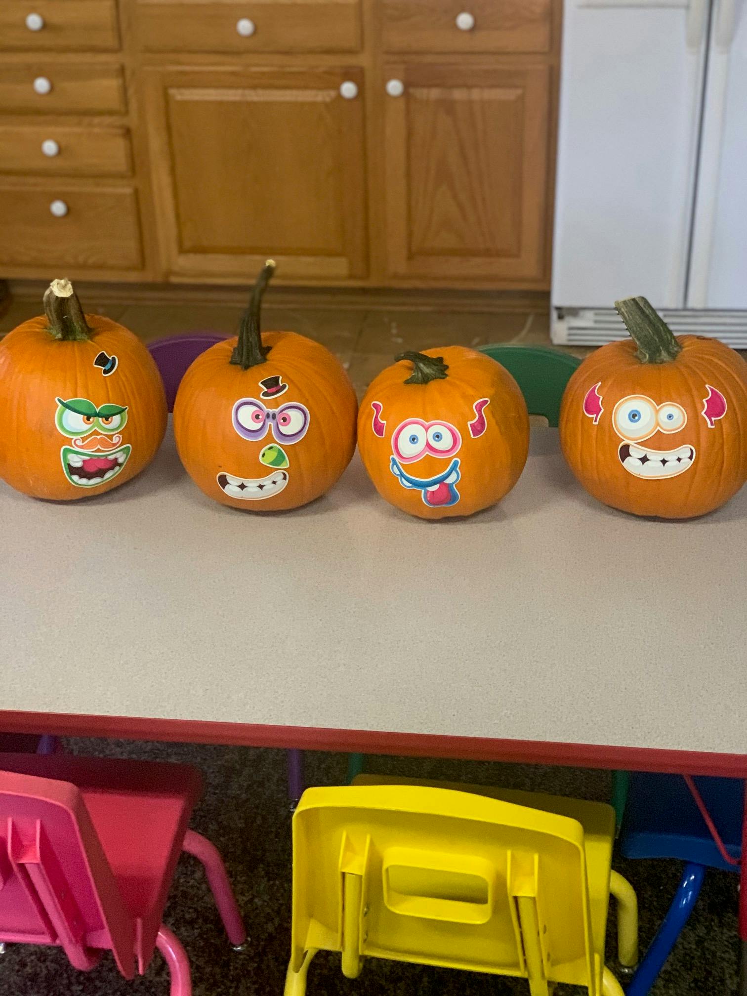 Four pumpkins decorated with sticker faces on a table