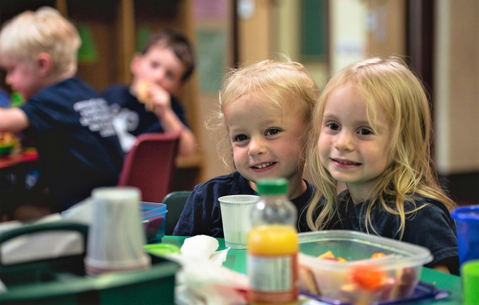 Two children sitting at a table with food and drinks