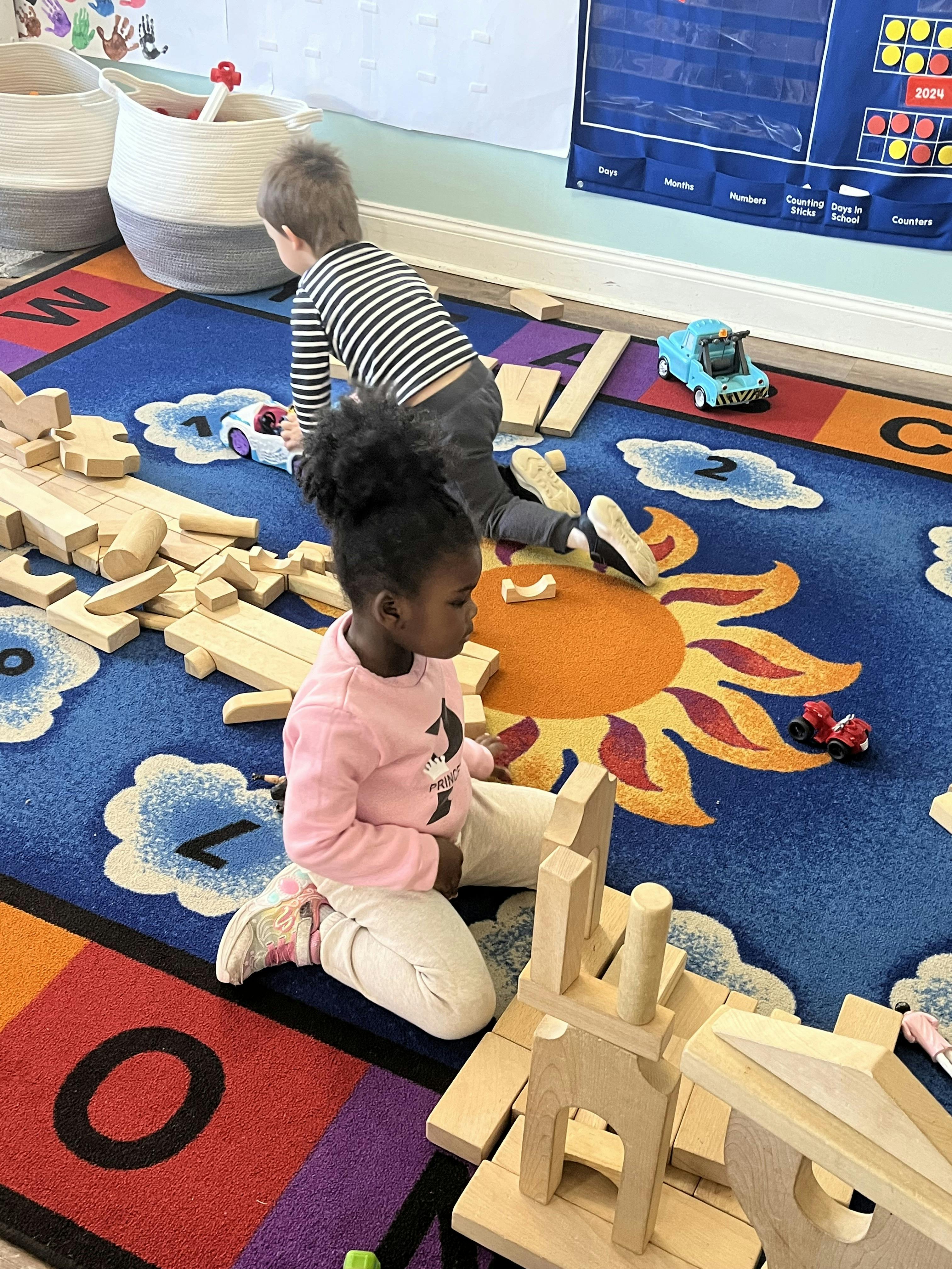 Two children playing with wooden blocks on a colorful rug in a classroom