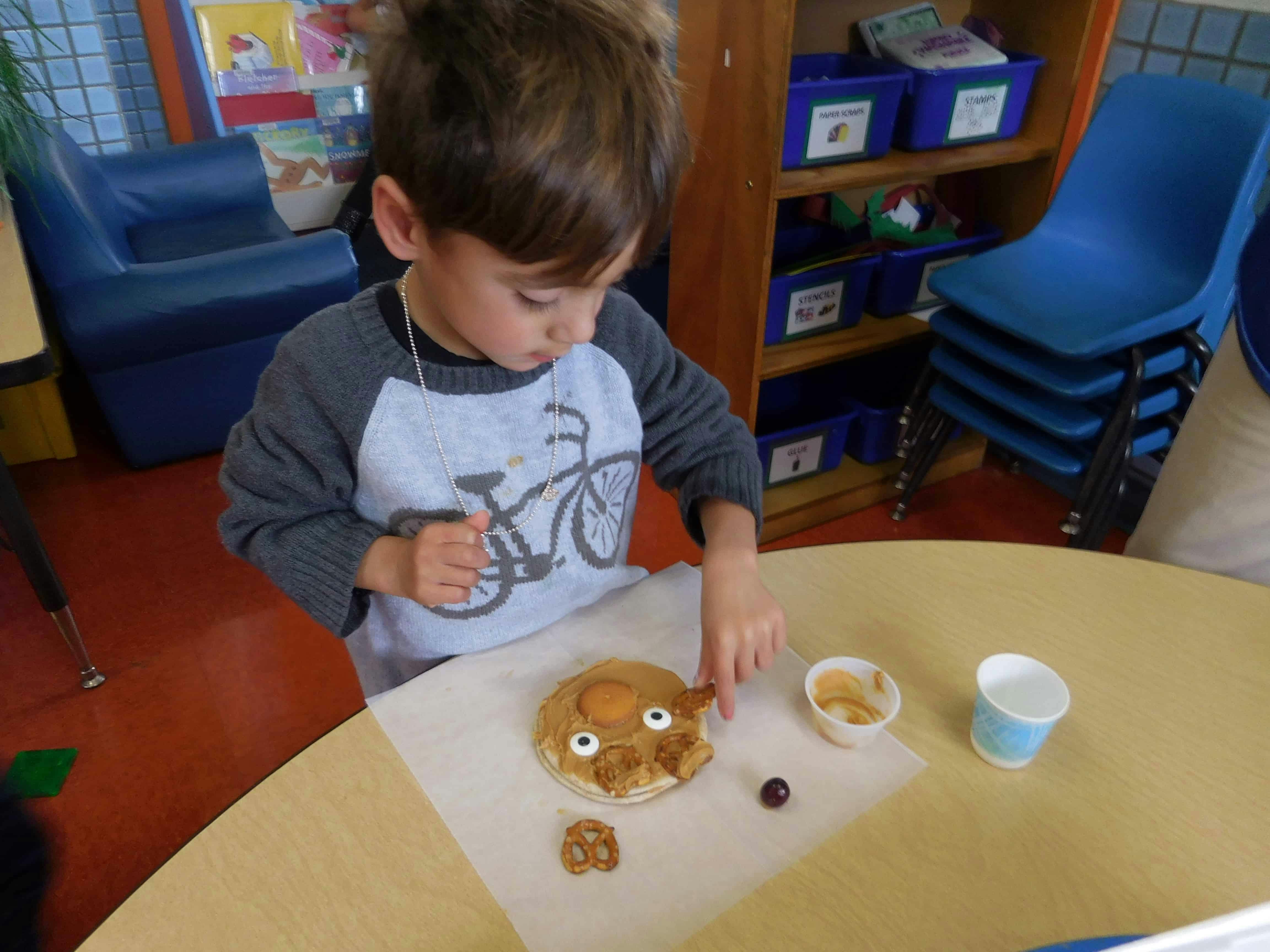 Child decorating a cookie with candy eyes and pretzels