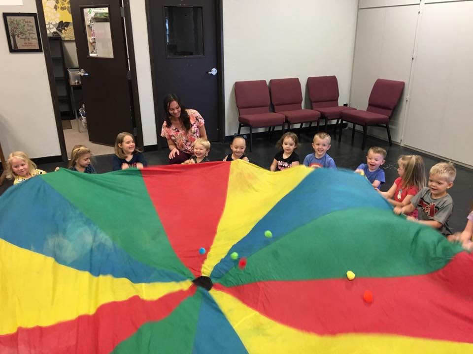 Adult and children playing with a colorful parachute in a room