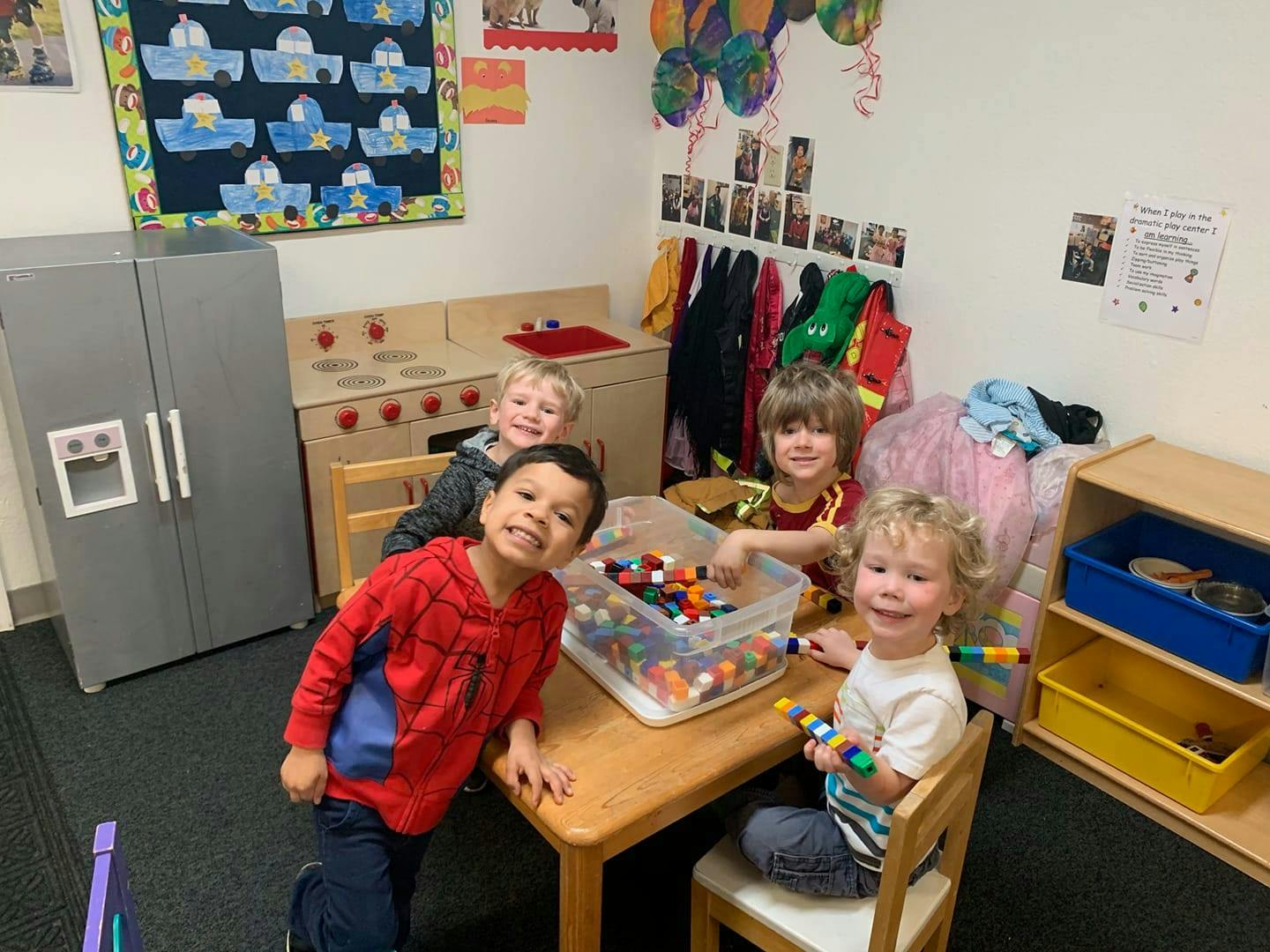 Four children playing with building blocks at a table in a classroom