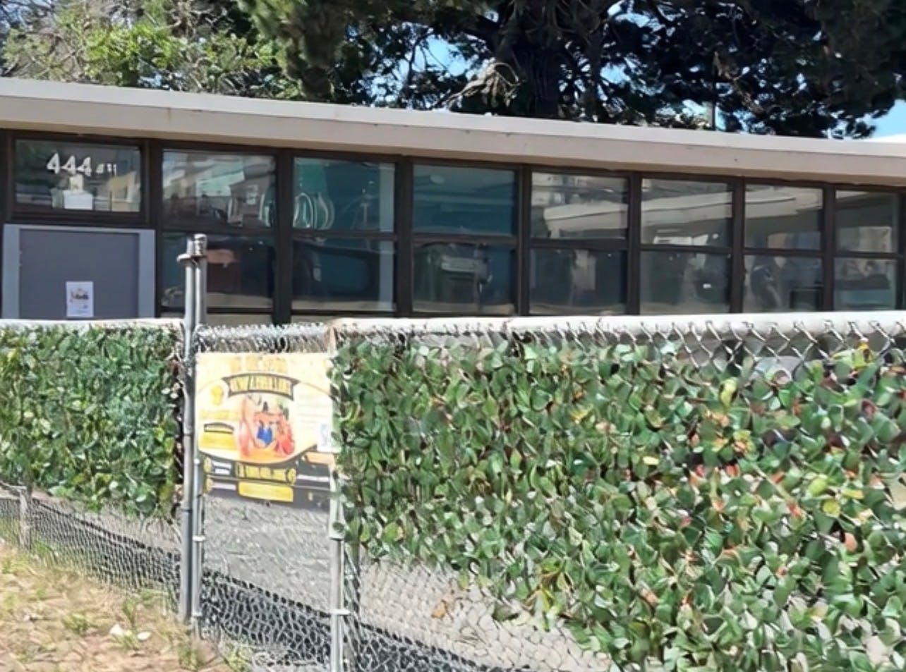 A chain link fence with green artificial foliage covering it, a building behind