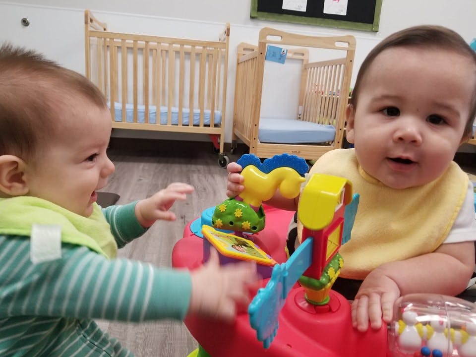 Two babies playing with a colorful toy in a room with cribs