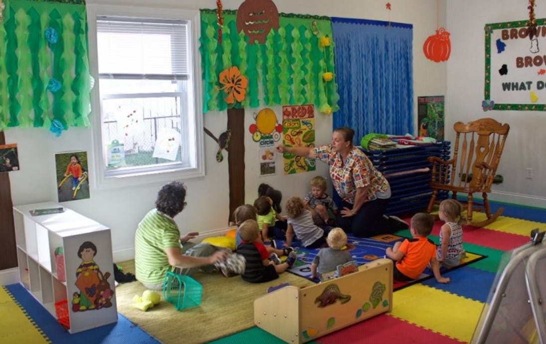 Two people with a group of children sitting on the floor in a classroom
