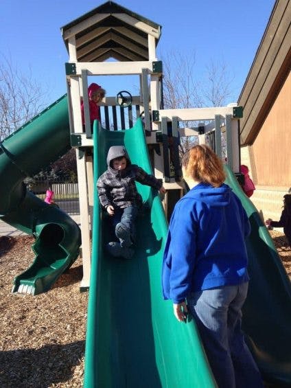 Child on a playground slide with a person standing nearby