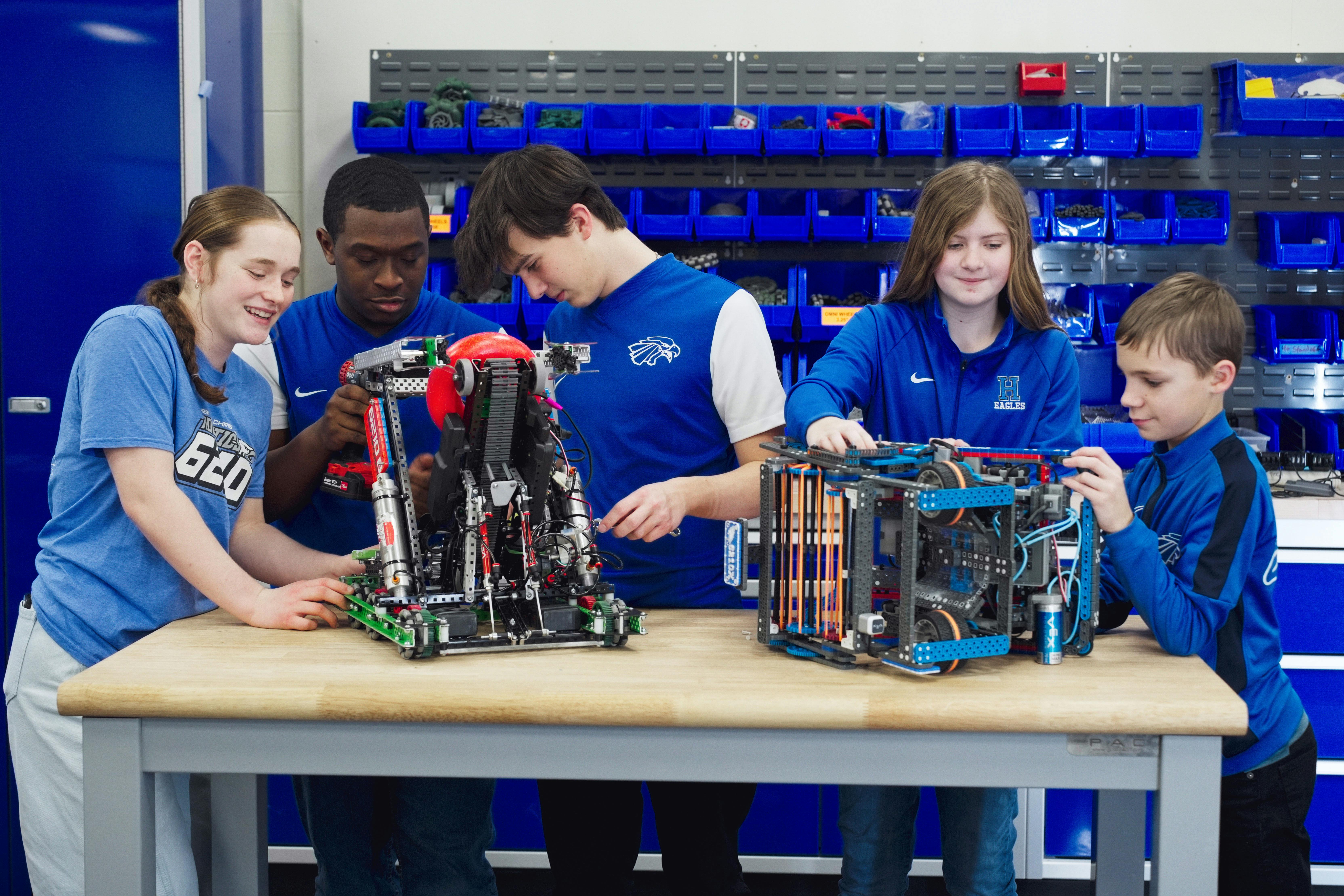 Four teens and children working on two robots on a table