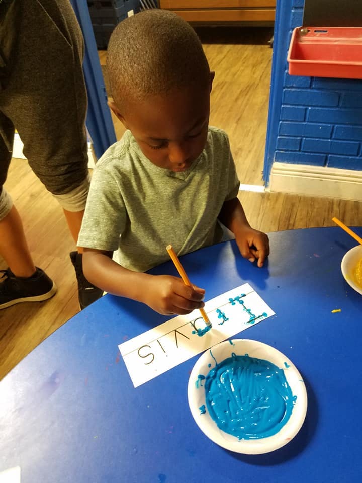 Child painting letters on paper with a brush