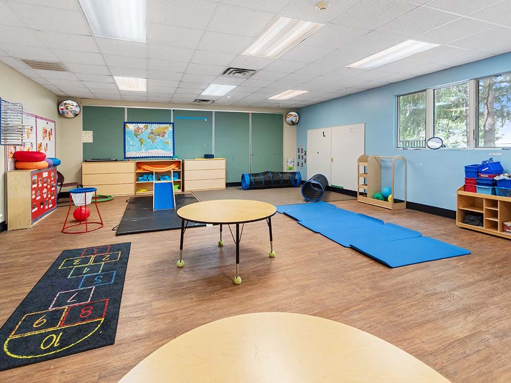 Classroom with hopscotch rug, blue mats, play tunnels, and small tables