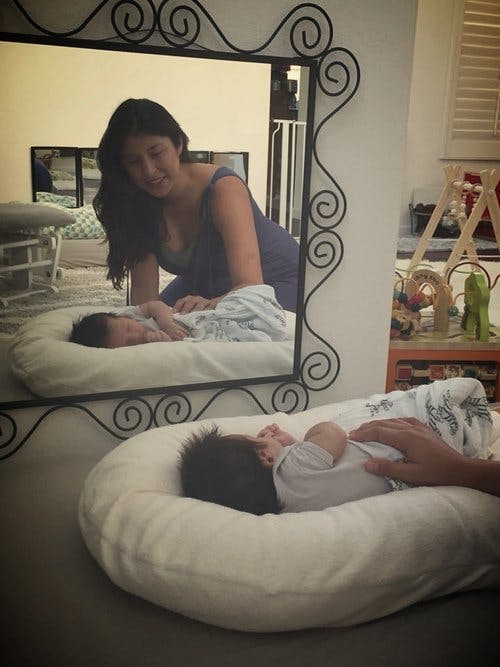 Person looking at a child sleeping in a baby nest, reflected in a mirror