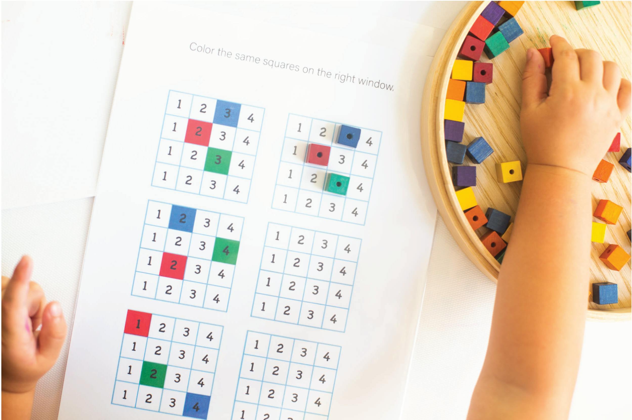Child's hands with a number puzzle worksheet and colorful blocks