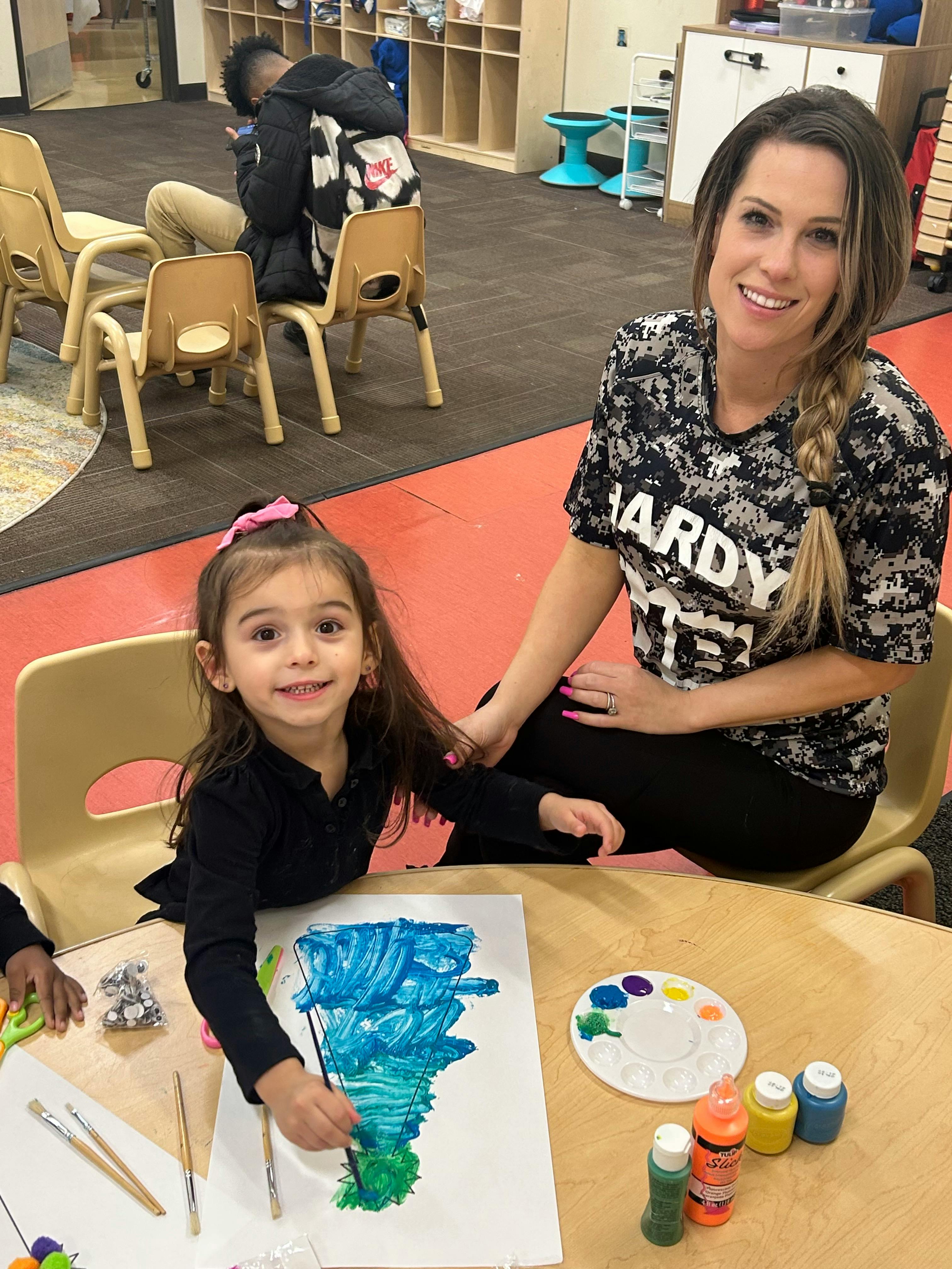 Adult and child painting at a table in a classroom
