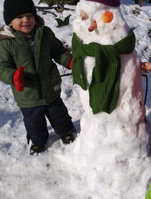 Child standing next to a snowman