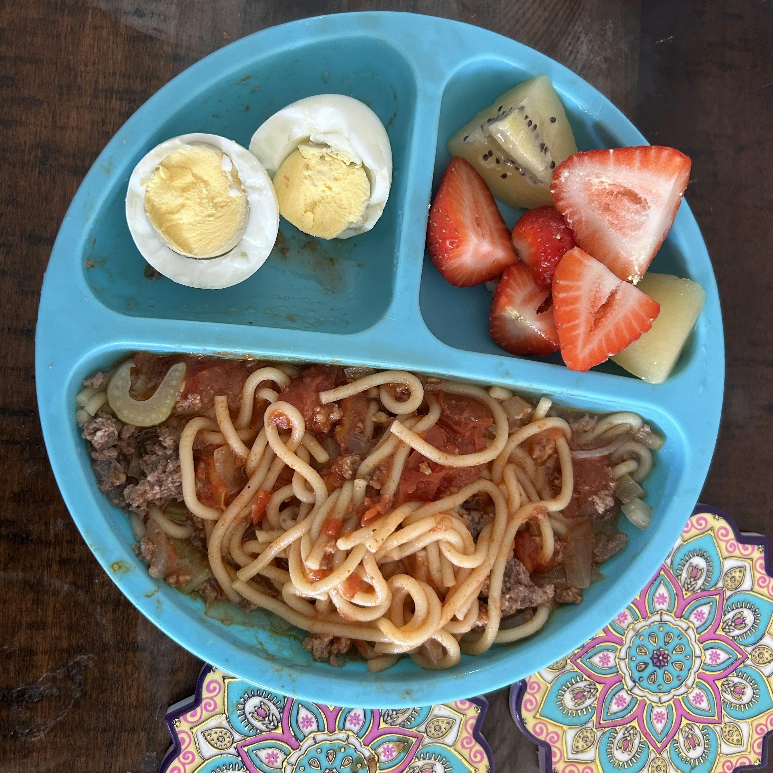 Spaghetti with meat sauce, sliced hard-boiled egg, and cut fruit on a plate