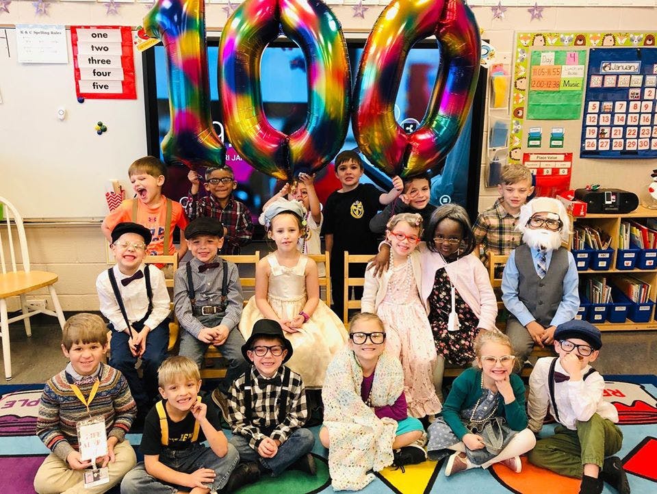 Group of children dressed in costumes in a classroom with large 100 balloons