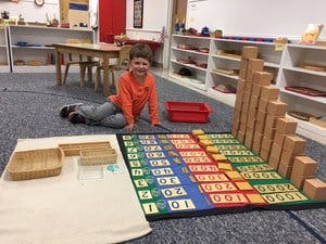Child sitting on floor next to a large block tower and a number mat