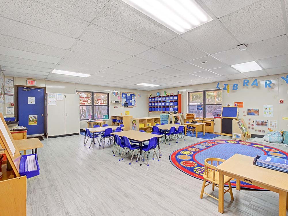Classroom with child-sized tables and chairs, an easel, and a reading nook