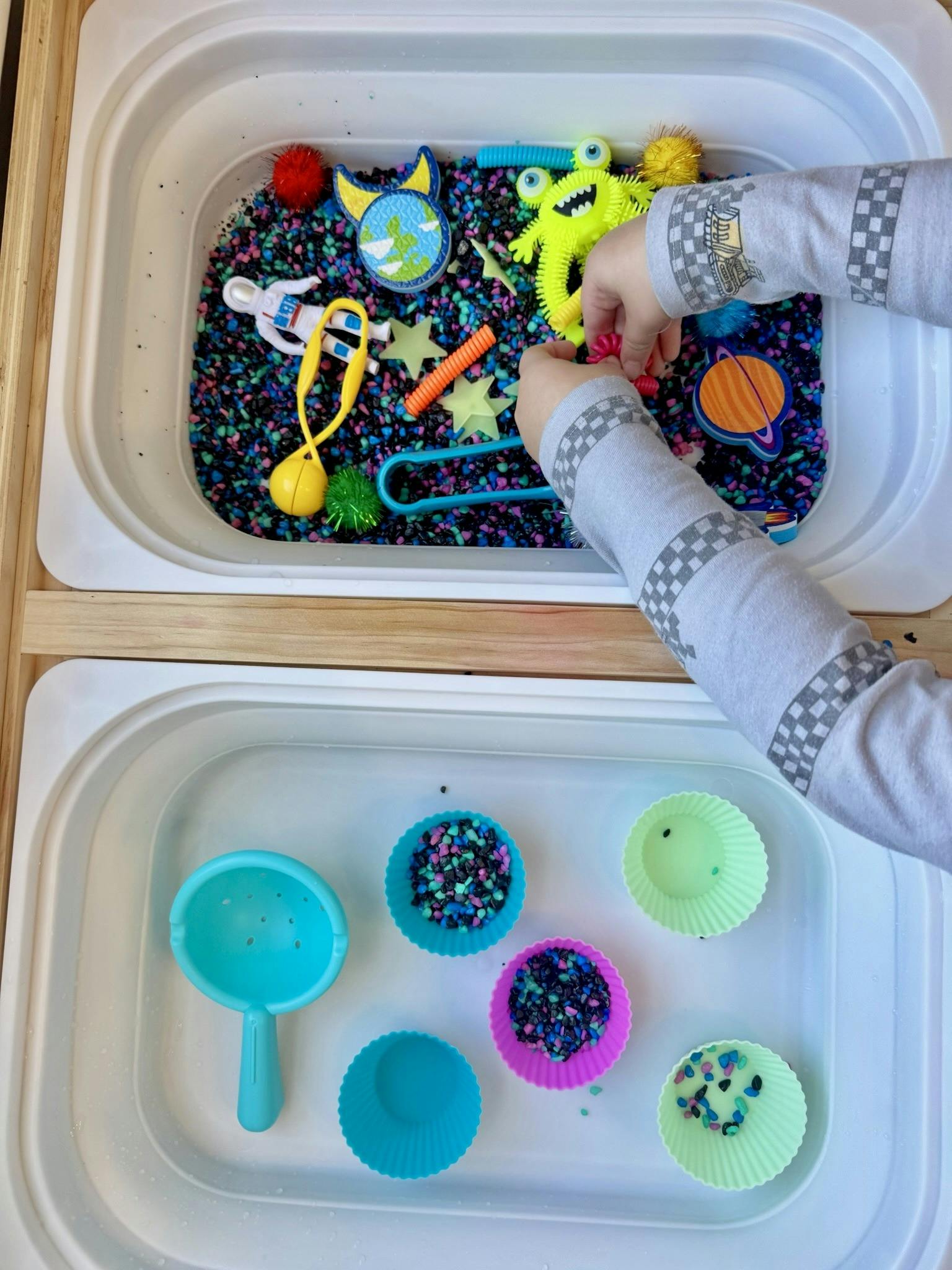 Child playing with space-themed sensory bin and colorful silicone cups
