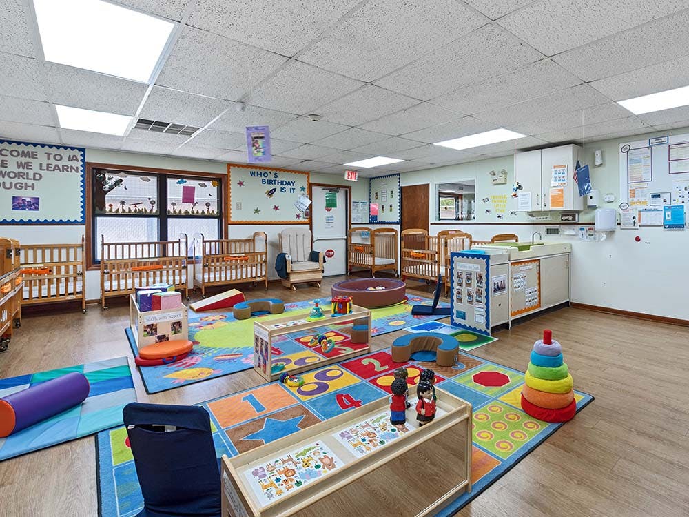 daycare classroom with multiple cribs, a changing station, and colorful playmats