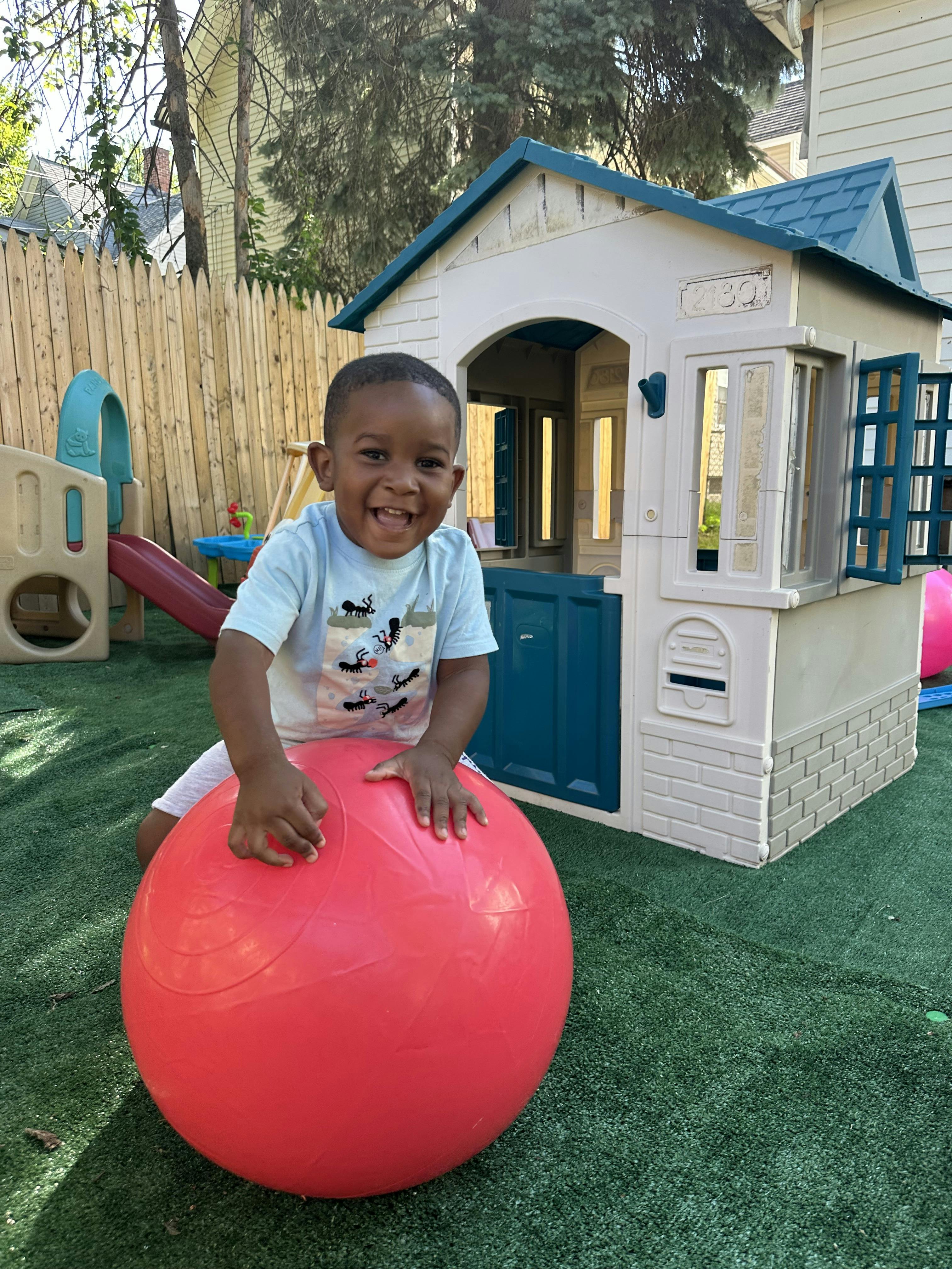 Child sitting on a large red ball in a play area
