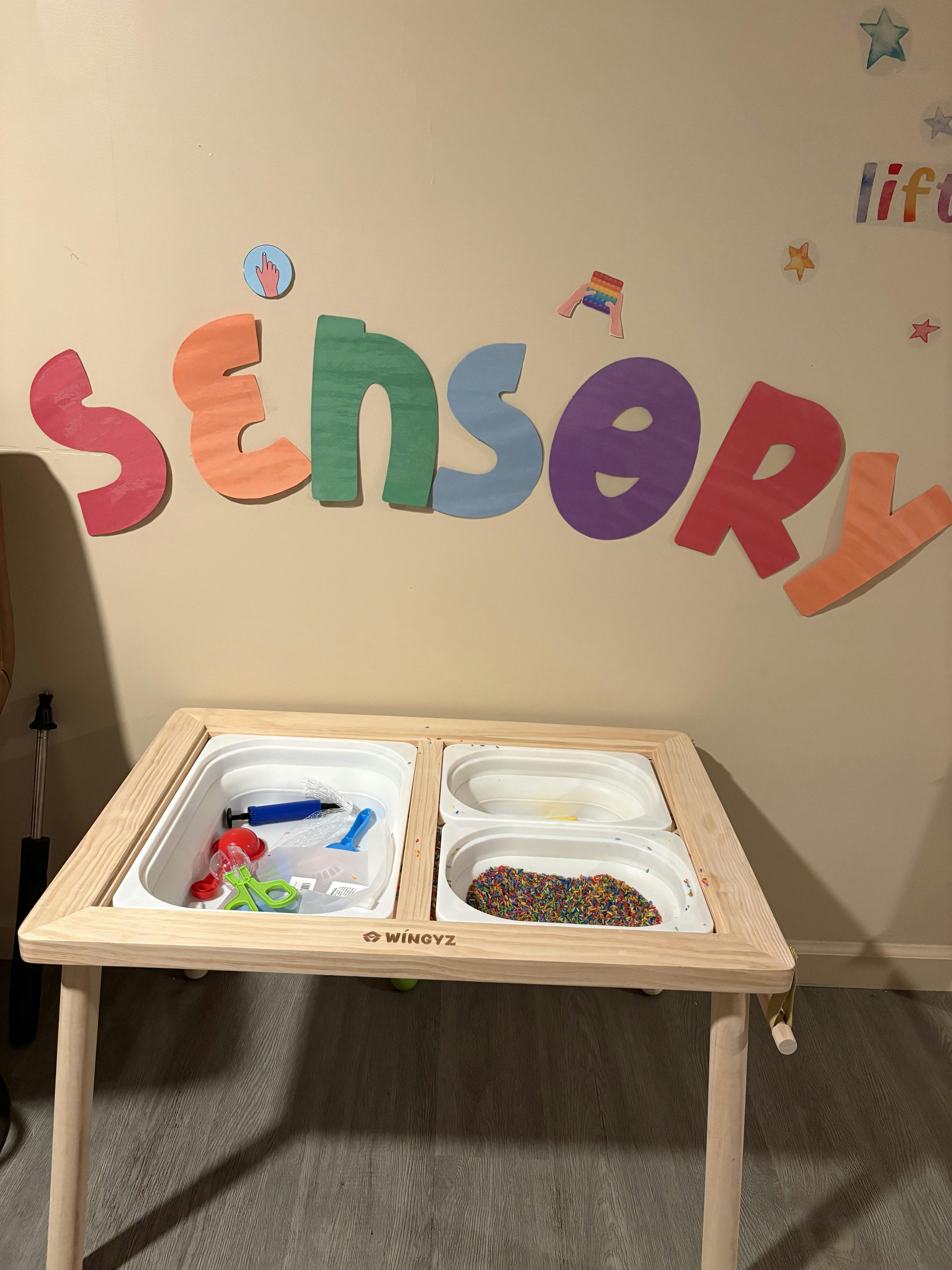 Wooden sensory table with bins of colorful rice and play tools