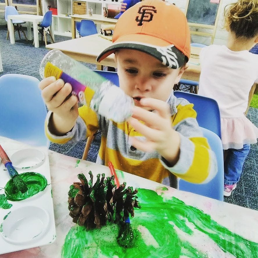 Child painting a pinecone green with green paint