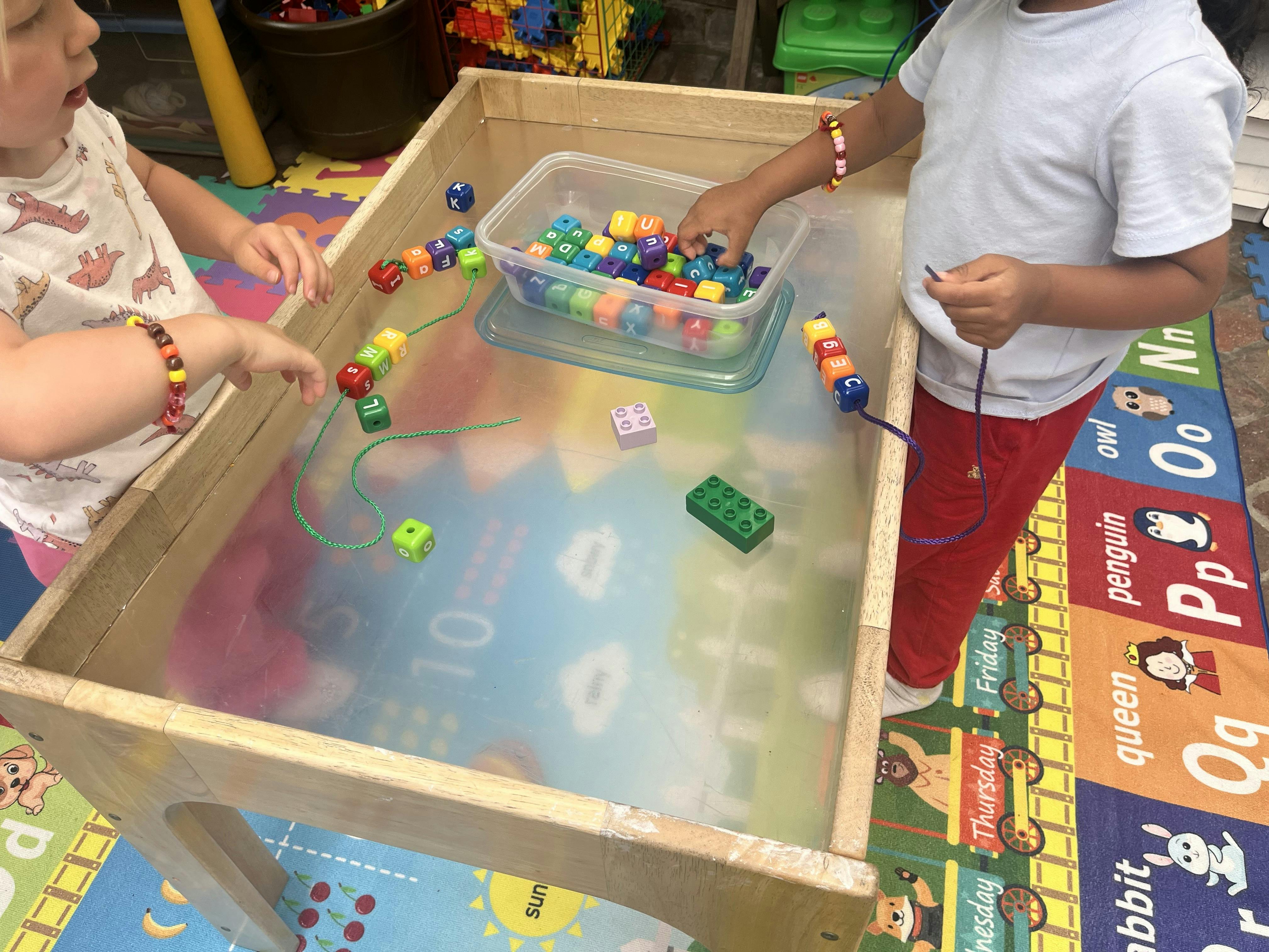 Children threading letter beads onto strings at a classroom activity table