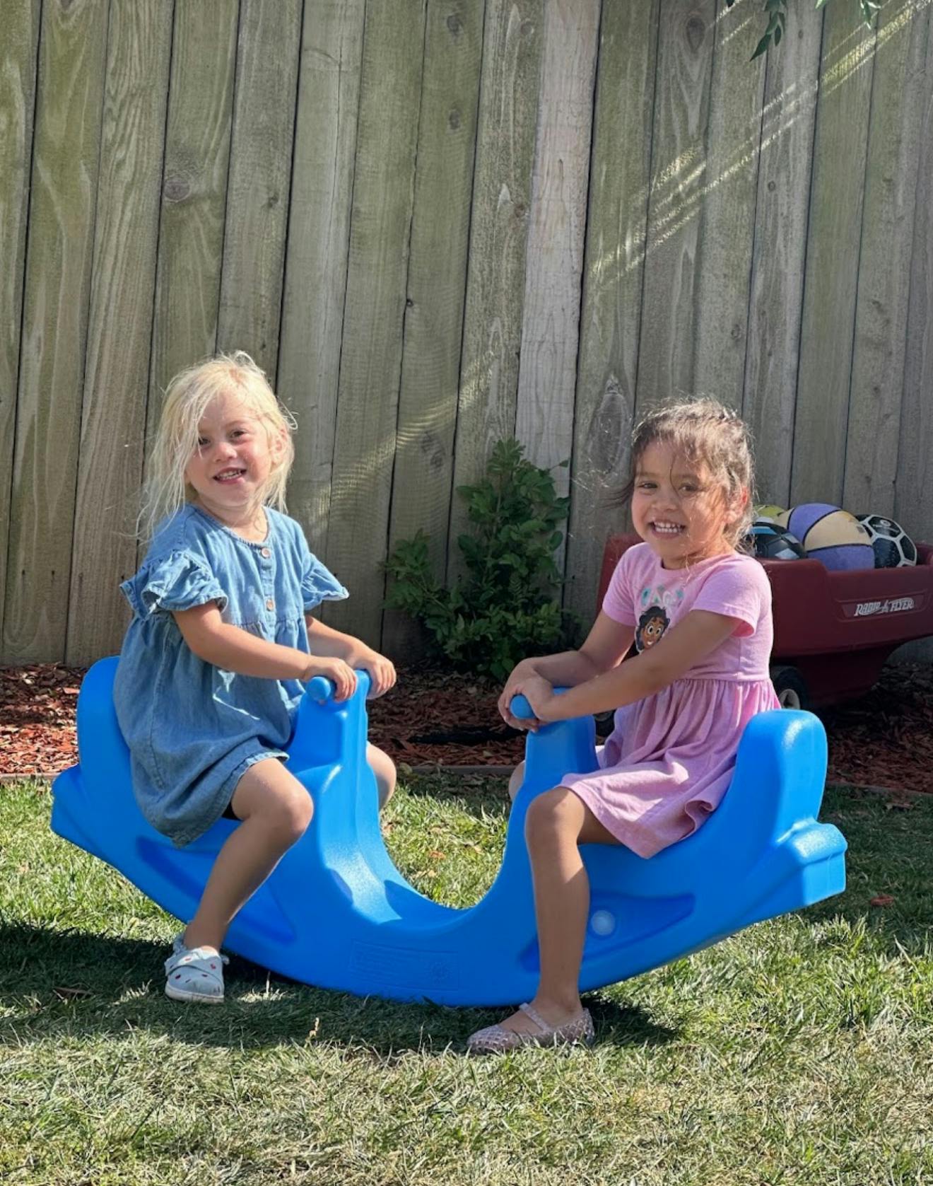 Two children playing on a blue plastic seesaw on a lawn