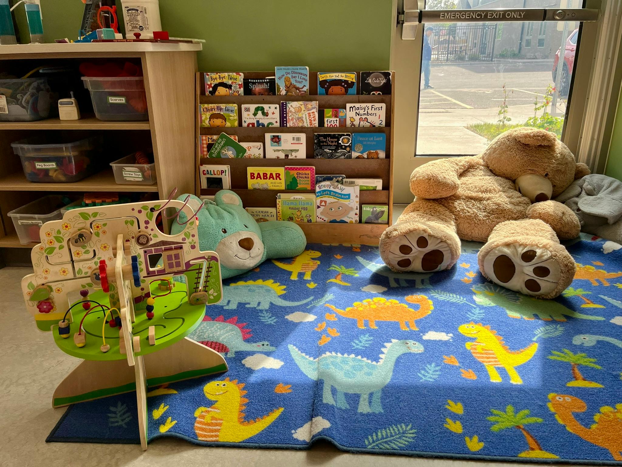 Children's play area with a dinosaur rug, stuffed animals, and a bookshelf
