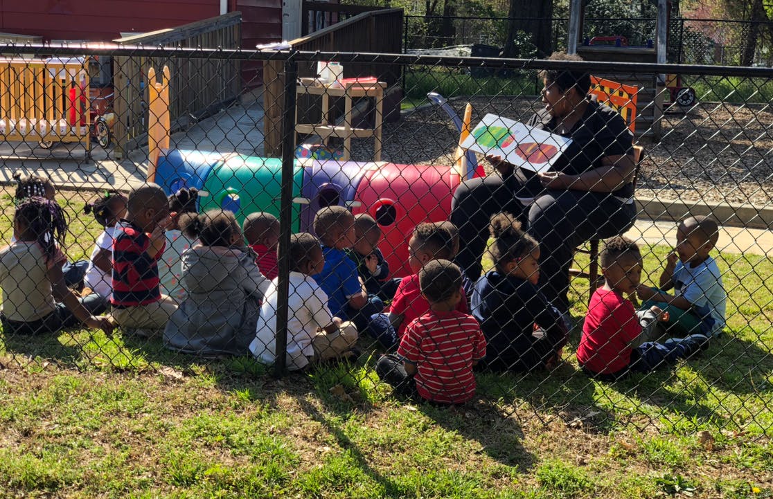 Person reading a book to a group of children outdoors